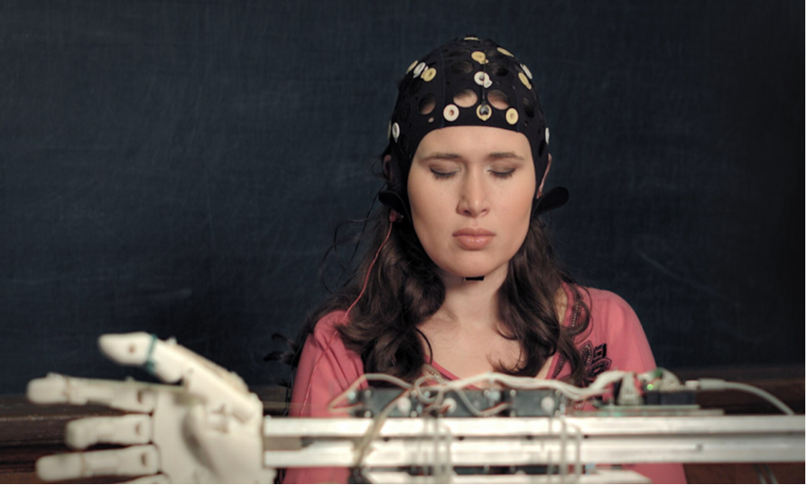 Image of a woman wearing an EEG cap as a part of a BCI to operate a robotic arm