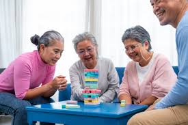 A group of elderly people gathered around a table, smiling and laughing, playing a game of Jenga. 