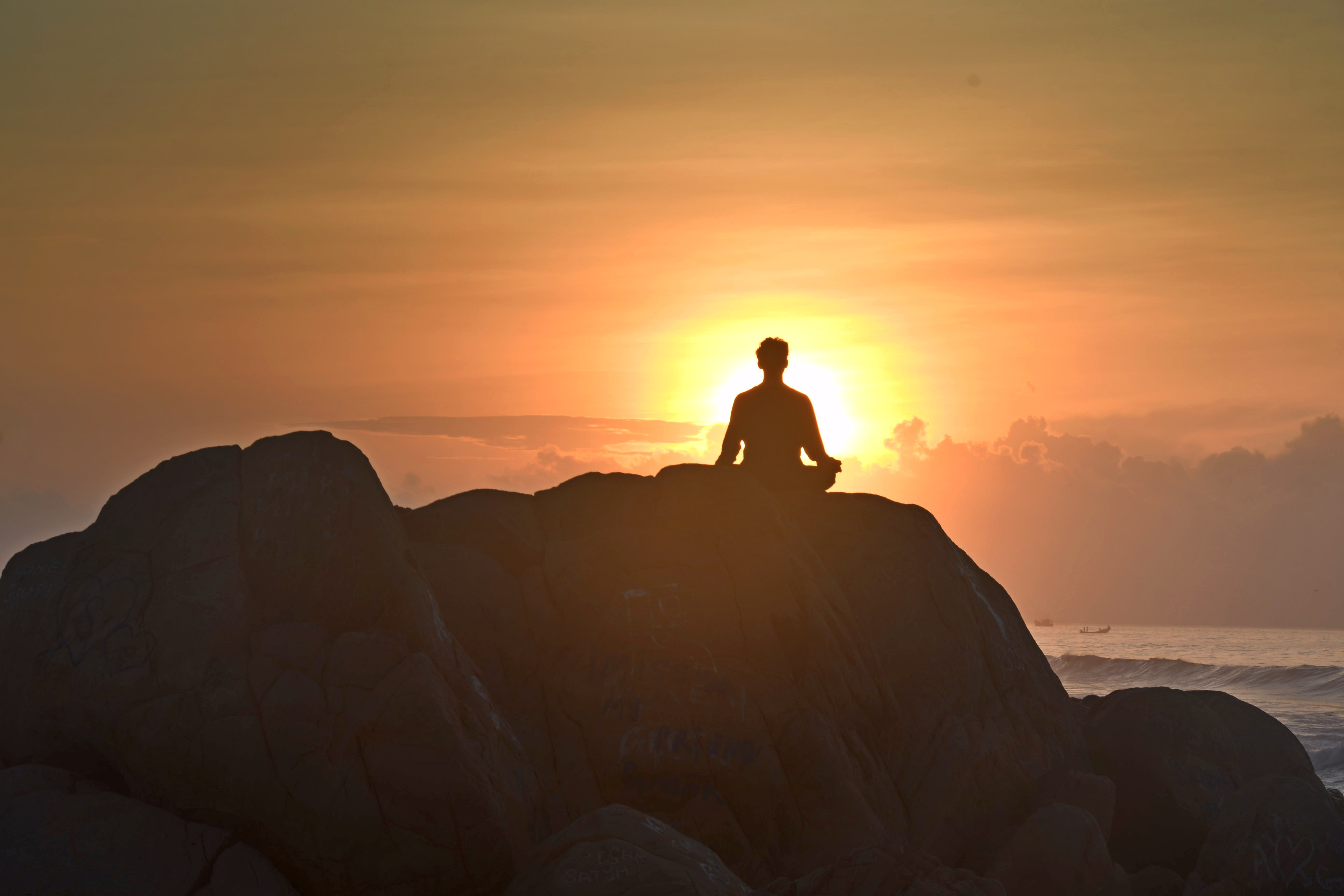 This is the image of someone sitting and meditating on a rock.