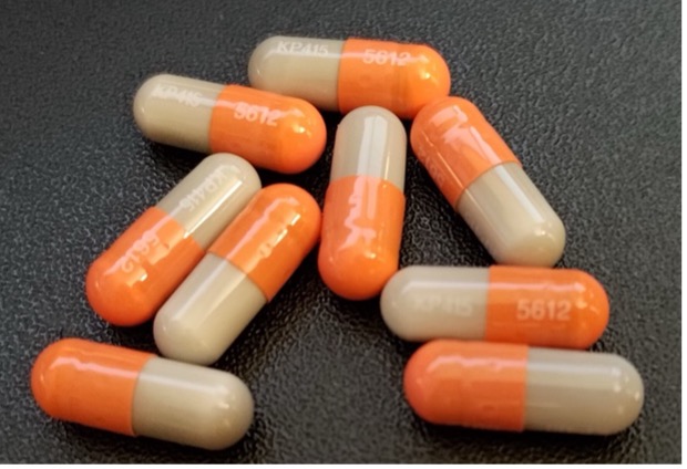 A group of pills that are half white and orange on a dark background.